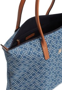 Μπλε τσάντα ώμου με σχέδιο και καφέ δερμάτινες λαβές, μερικώς ανοιχτό φερμουάρ στην κορυφή που αποκαλύπτει το σκοτεινό εσωτερικό και εσωτερική τσέπη με φερμουάρ.
