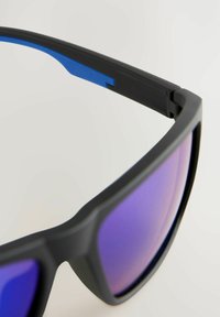 Ochelari de soare negri cu un finisaj mat, având lentile cu gradient mov și accente albastre pe brațe. Design aerodinamic și unghiular.