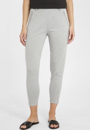 Lichtgrijze broek van zacht materiaal, met voorste ritsen, slim fit ontwerp en een cropped lengte, gecombineerd met zwarte schuifsandalen.
