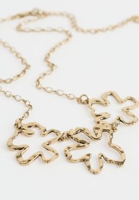 Halskette aus goldfarbenem Metall mit drei blütenförmigen Anhängern im gewellten Design, verbunden durch eine zarte Kette. Glatte Textur mit glänzender Oberfläche.