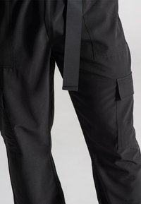 Czarne spodnie bojówki wykonane z gładkiego materiału o luźnym kroju, z paskiem, bocznymi kieszeniami i prostym designem, zapewniającym funkcjonalność.