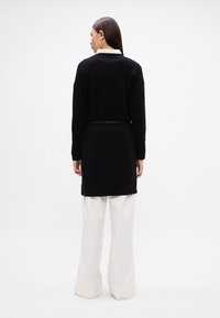 Μαύρο πλεκτό πουλόβερ με χαλαρή εφαρμογή, διαθέτει μακριά μανίκια και στρογγυλή ραφή. Συνδυάζεται με άσπρα παντελόνια με ψηλή μέση και φαρδύ πόδι.