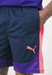 Marinefarbene Sportshorts mit einem pinken Puma-Logo. Sie haben einen Farbverlauf von Marineblau zu leuchtendem Pink und ein strukturiertes Muster am Saum.