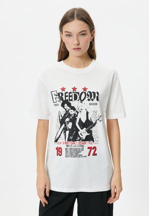 Camiseta de algodón blanca con un gráfico impreso en negro y rojo de músicos, texto y fechas, con mangas cortas y un corte holgado.