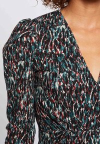 Robe noire avec un motif abstrait multicolore ; présente un décolleté en V profond et des manches bouffantes froncées. Le tissu semble texturé et léger.