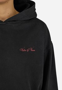 Moletão preto com texto em cursivo vermelho "Valores & Visões" no peito, usado por uma pessoa mostrada do pescoço até a parte superior do torso, fundo branco.