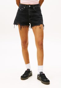 Svarte denimshorts med frynset kant, høy midje og slitte detaljer. Brukt med svarte joggesko og hvite ankle-sokker.