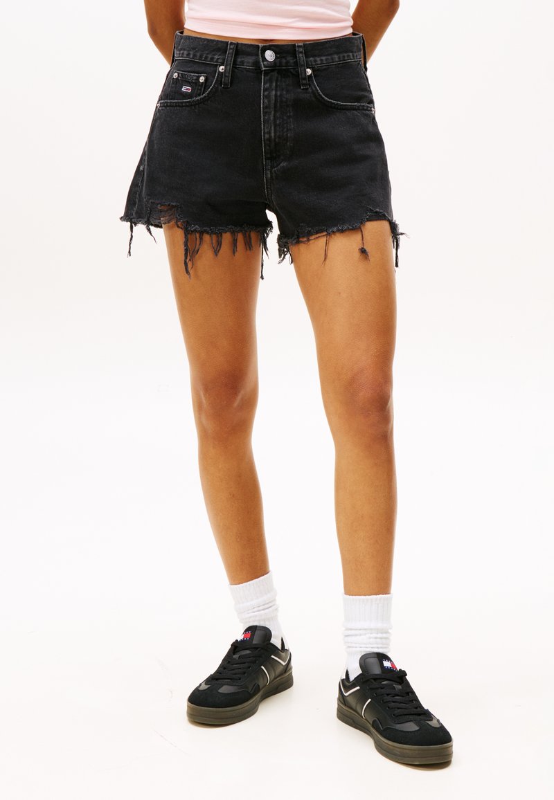 Svarte denimshorts med frynset kant, høy midje og slitte detaljer. Brukt med svarte joggesko og hvite ankle-sokker.