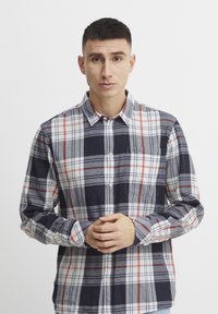 Camisa de botones con patrón de cuadros, en colores azul marino, rojo y blanco. Manga larga, cuello y bolsillo en el pecho con textura de tela suave.