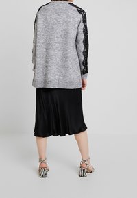 Grijze gebreide trui met zwarte kantaccenten, gedragen over een zwarte satijnen rok. De look wordt compleet gemaakt door sandalen met hoge hakken in zebraprint.