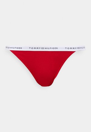 Piros tanga, fehér derékrésszel, amelyen a "TOMMY HILFIGER" felirat fekete színben található. Az anyag sima tapintású és testhez simuló fazonú.
