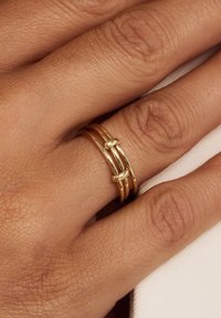 Gouden metalen ringenset met drie in elkaar grijpende banden met gladde oppervlakken en een gepolijste afwerking, die een minimalistisch ontwerp laat zien.