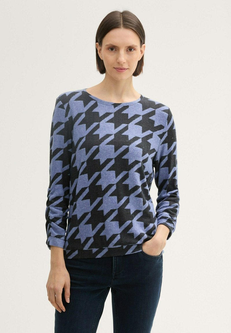 Blaue und schwarze Hundezahn-Muster Pullover aus weichem Strickstoff, mit rundem Ausschnitt und langen Ärmeln, kombiniert mit dunklen Jeans.