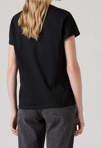 Camiseta de algodón negra de manga corta, con escote redondo y un corte relajado. Se combina con unos pantalones vaqueros gris oscuro de cintura alta.