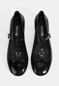 Schwarze Lackleder-Ballettflats mit einem T-Riemen-Design, das mit einer goldenen Schnallenakzent und einer glatten, glänzenden Oberfläche versehen ist.