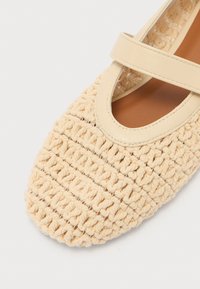 Zapato plano de ganchillo beige con punta redonda, que presenta una correa de cuero cruzando el empeine y un forro interior suave.