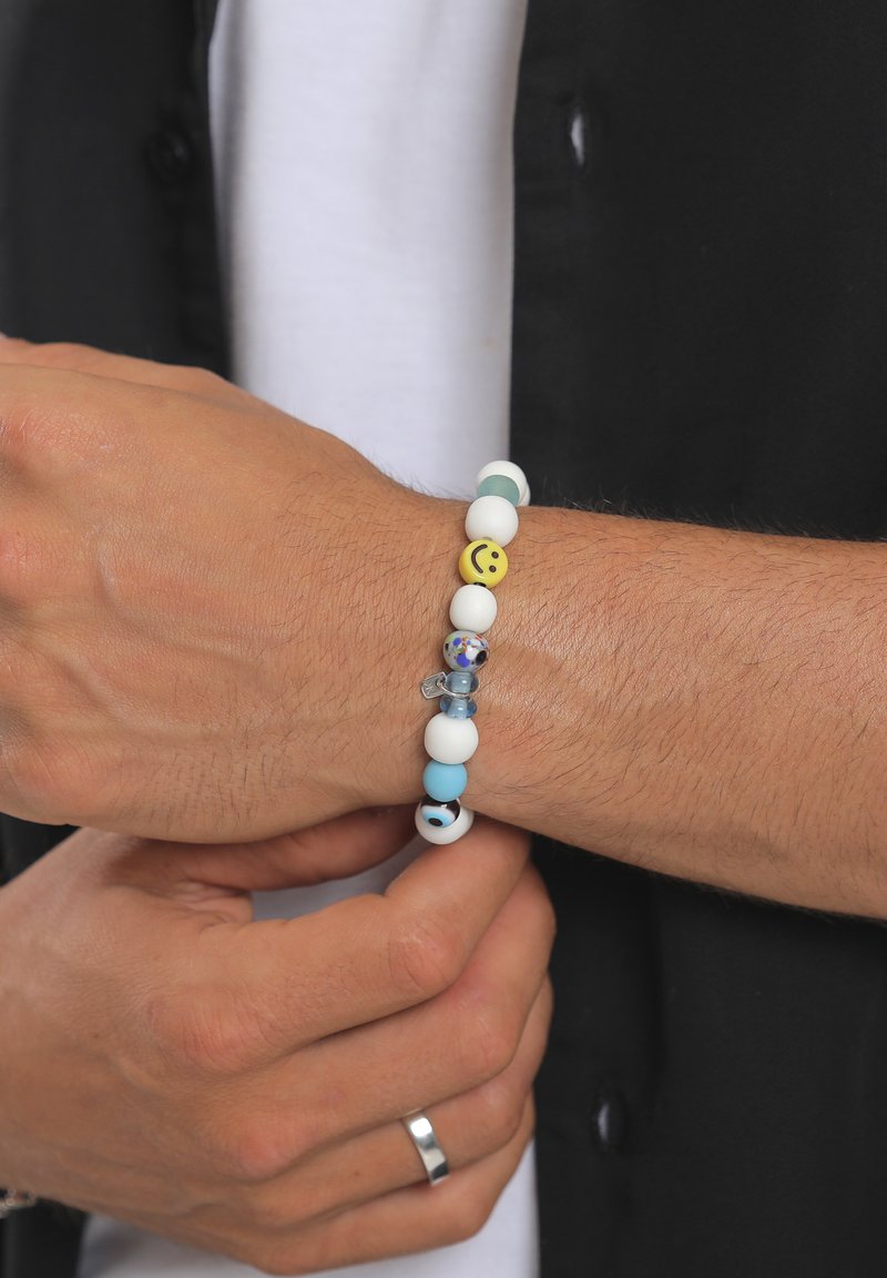 Bracelet multicolore en perles comprenant des perles blanches, bleu clair et vertes, un pendentif smiley jaune et des accents en verre.