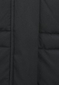 Μαύρο καπιτονέ ύφασμα με κάθετη ραφή και λείο επενδυμένο πάνελ, που παρουσιάζει λεπτομερή υφή και ραφές.