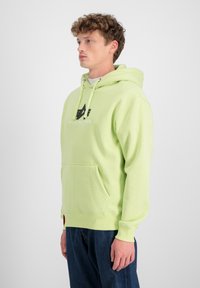 Sudadera verde clara con bolsillo canguro, capucha con cordones y detalles de logo. Tejido de mezcla de algodón, corte relajado, puños y dobladillo acanalados.