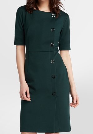 Robe vert foncé jusqu'aux genoux avec manches courtes, ornée d'une rangée verticale de grands boutons circulaires noirs et argentés sur le devant.