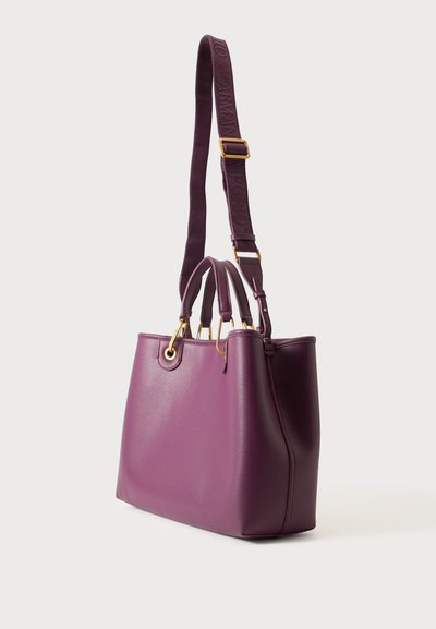 Sac à main en cuir violet avec deux poignées courtes, une large bandoulière réglable avec texte logo et des accents métalliques dorés.