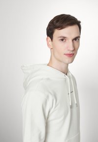 White hoodie with a front pocket, drawstrings, and subtle branding. Smooth texture, relaxed fit, and a classic design.