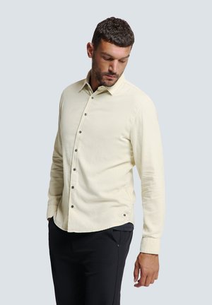 Lichtbeige overhemd met lange mouwen, zachte textuur en donkere knopen. Draagt met zwarte broek, die een minimalistisch ontwerp toont.