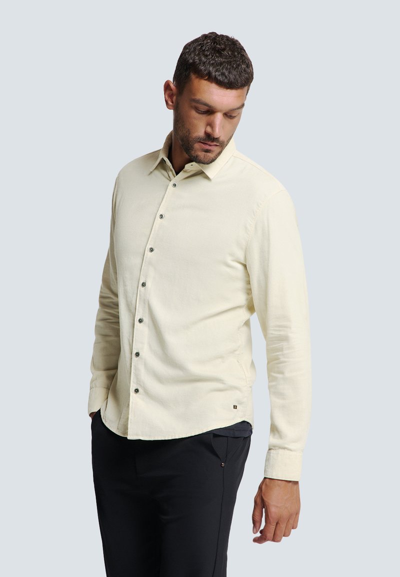 Lichtbeige overhemd met lange mouwen, zachte textuur en donkere knopen. Draagt met zwarte broek, die een minimalistisch ontwerp toont.