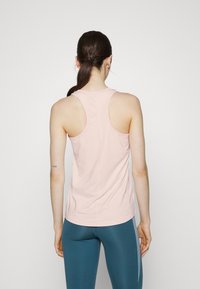 Débardeur sportif rose clair avec un design dos nageur, fabriqué en matériau lisse et extensible. Présente une silhouette ajustée et des coutures minimales.