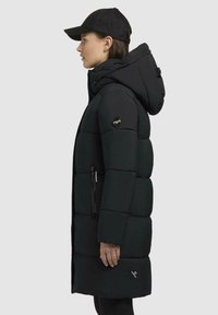 Zwarte padded jas met capuchon, met een geborduurd ontwerp, ritszakken en een logo-detail op de mouw; gladde, matte textuur.