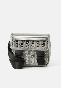 Sølv messenger-veske med geometrisk relieffmønster, justerbar svart reim, magnetisk klafflukking og logodetalj på forsiden.