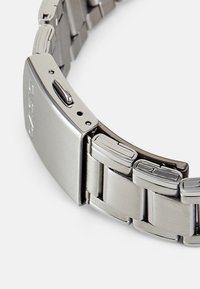 Silver stainless steel watch bracelet featuring a flat design, rectangular links, and a clasp with a polished finish and engraved logo.