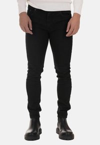 Black skinny jeans made of denim, featuring a smooth texture. Paired with black leather ankle boots with a chunky sole.