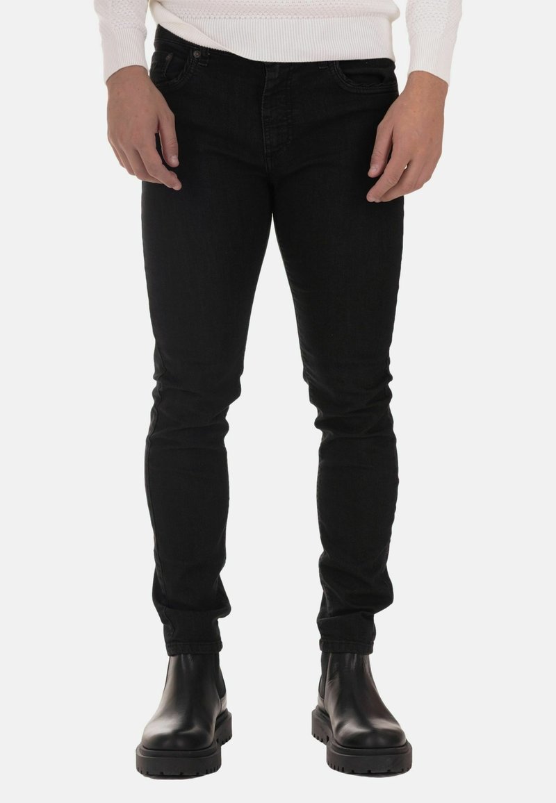 Black skinny jeans made of denim, featuring a smooth texture. Paired with black leather ankle boots with a chunky sole.
