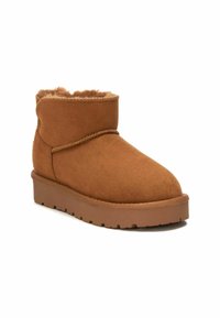 Stivaletto in camoscio marrone con rivestimento morbido, punta rotonda e suola in gomma con motivo a zigzag. Dettaglio di cucitura lungo la tomaia.
