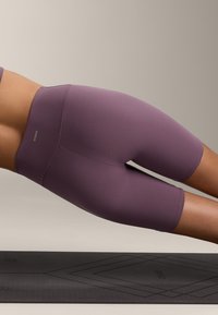 Lila, magas derekú kerékpáros sort, sima, rugalmas anyagból, egyszínű kivitelben, amelyen a derekán logó található.