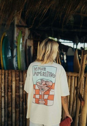 Kremowy, oversize'owy t-shirt z graficznym nadrukiem napoju z krewetkami na szachownicowym tle, z napisem "WAVE APERITIVO".
