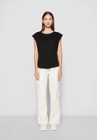Top negro de manga corta con escote redondo combinado con pantalones cargo marfil que tienen bolsillos laterales y un silueta relajada. Zapatillas blancas.