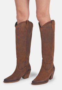 Bottes en cuir marron, hauteur genou, avec un bout pointu et une finition texturée, dotées d'un talon empilé et de languettes sur les côtés pour un enfilage facile.