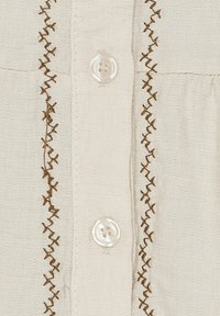 Creme knap-op blouse med brun broderet detalj langs stolpen. Har klare plastikknapper og et blødt, tekstureret stof.