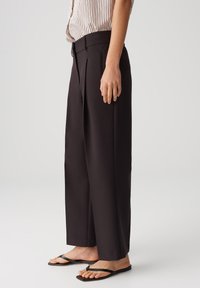 Black, high-waisted trousers with a wide-leg design. Made from smooth fabric, featuring sharp front pleats and a tailored fit.