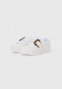 White sneakers with a smooth leather upper, featuring a gold buckle detail, lace-up front, and textured rubber sole with branding.