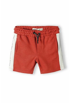 Shorts en coton rouge avec une taille élastique, cordon noir, poches latérales et panneaux latéraux blancs comportant du texte. Texture lisse.