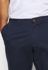 Navy blue cotton pants with a smooth texture, featuring side pockets and a button closure. Minimalistic design with subtle stitching details.
