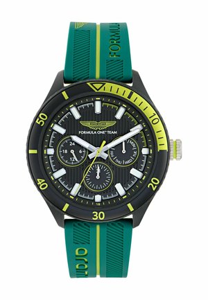 Juodas laikrodis su tekstūruotu ciferblatu ir trimis subdials. Yra žalios gumos juosta su geltonais akcentais ir ryškiais baltais valandų žymekliais.