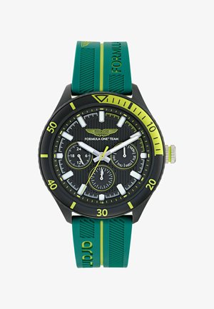 Juodas laikrodis su tekstūruotu ciferblatu ir trimis subdials. Yra žalios gumos juosta su geltonais akcentais ir ryškiais baltais valandų žymekliais.