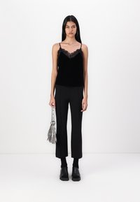 Black velvet camisole with lace trim, paired with black tailored pants. Model holding a silver handbag, wearing chunky black clogs.