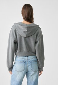 Kort grijs hoodie met een gestructureerde stof, oversized mouwen en een capuchon met trekkoord, gecombineerd met lichtblauwe spijkerbroek.