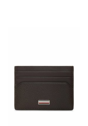 Mørkebrun læderkortholder med tre kortlommer og et lille rektangulært metallogo med røde, hvide og sorte striber.