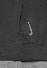 Camiseta deportiva negra con un sutil patrón texturizado; presenta un logotipo de Nike en gris en el frente. La tela parece ligera y transpirable.